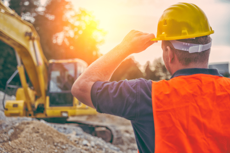Construction worker in hard hat observing equipment, emphasizing workplace safety and construction site activity.