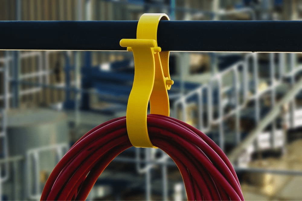 A yellow clip connected to a pipe, featured as the OktoLock® multipurpose safety clip for secure attachment.