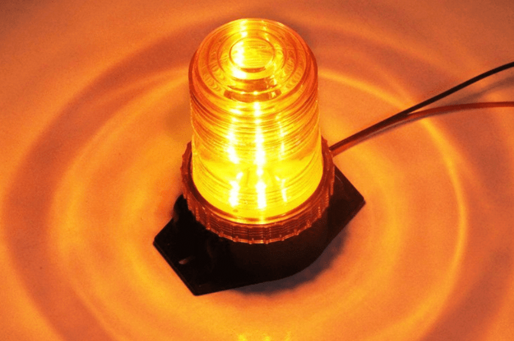 A yellow strobe light illuminates a surface, serving as a workplace warning signal.