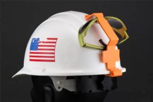 A hard hat with Goggle Guard® Clips holding a pair of safety goggles, showcasing a practical safety accessory combination