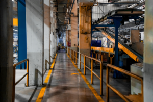 A long industrial hallway featuring yellow safety lines and metal railings, highlighting the need for industrial safety solutions for walkways.