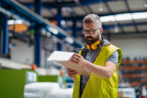A man in a safety vest holds a clipboard, reviewing OSHA safety gate requirements on a construction site.