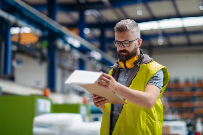 A man in a safety vest holds a clipboard, reviewing OSHA safety gate requirements on a construction site.